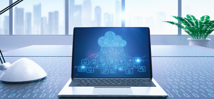 A laptop with a cloud computing illustration on the screen, placed on a desk with a cityscape in the background. Keyword.