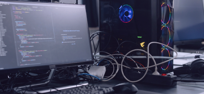 A sleek desktop computer setup featuring a monitor displaying code and a tower with colorful DDIL-branded fans, accompanied by neatly arranged cables and headphones resting on the desk.